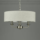 A modern cream fabric drum shade chandelier with three matte silver candle-style lights.