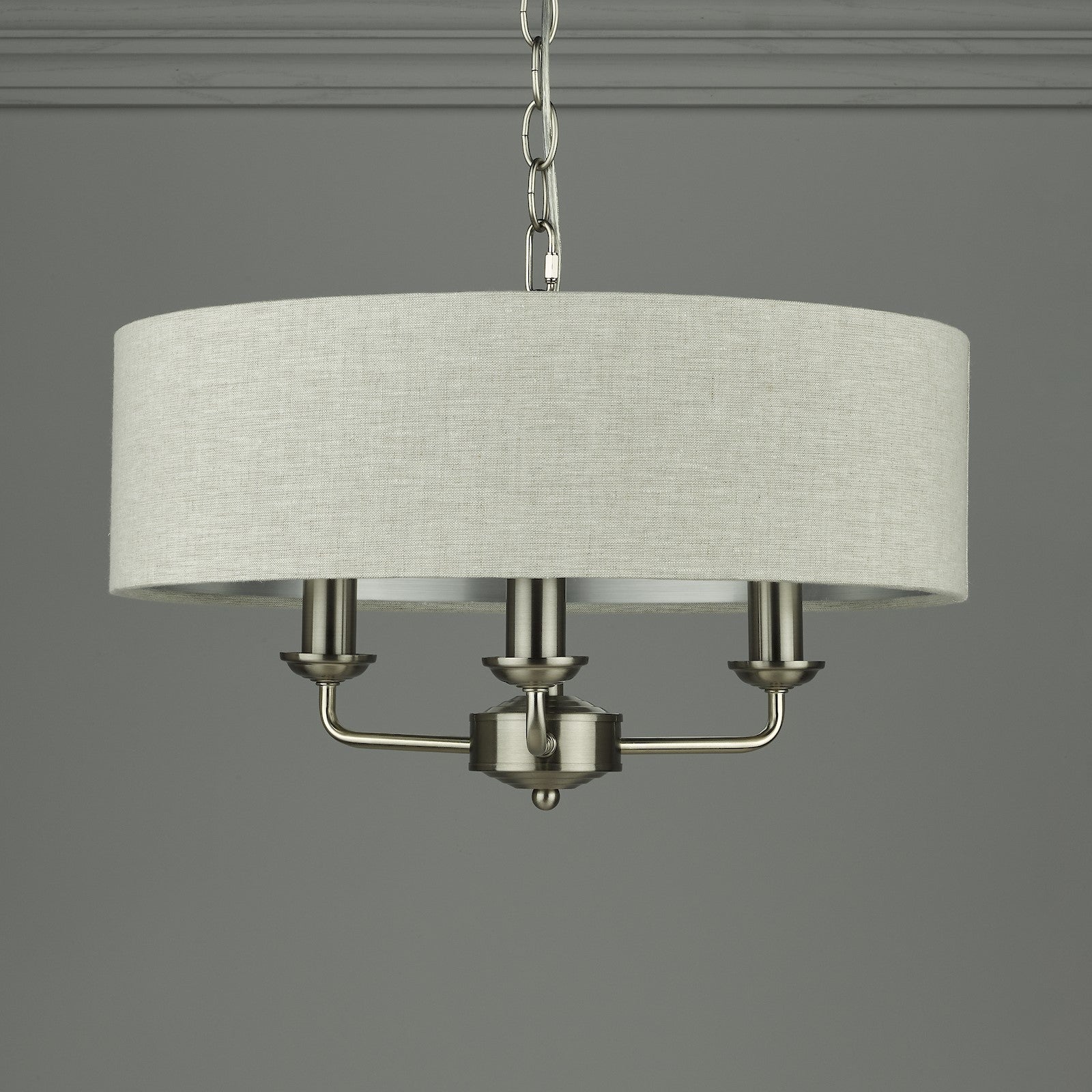 A modern cream fabric drum shade chandelier with three matte silver candle-style lights.