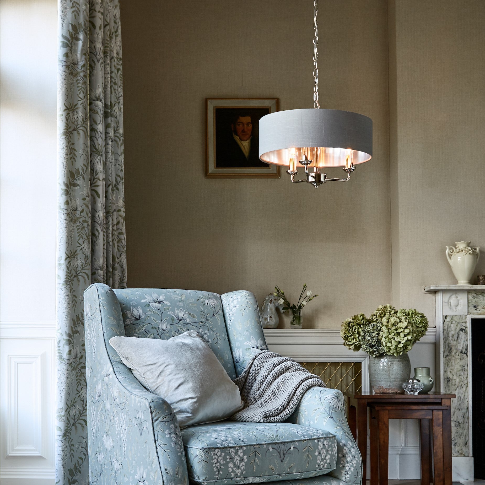 A cream drum shade chandelier with three candle-style lights illuminates a cozy living room.