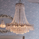 A close up view of a three-tier crystal chandelier in a home, with a mirror in the background.