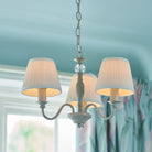 A three-arm chandelier with pleated shades in a light blue room.