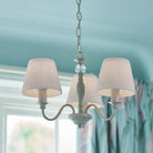 A three-arm chandelier with pleated shades in a light blue room.