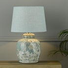 A decorative ginger jar lamp base with a pale blue lamp shade in a living room.