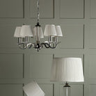 A chandelier with five pleated white lampshades hangs above a floor lamp with a matching shade.