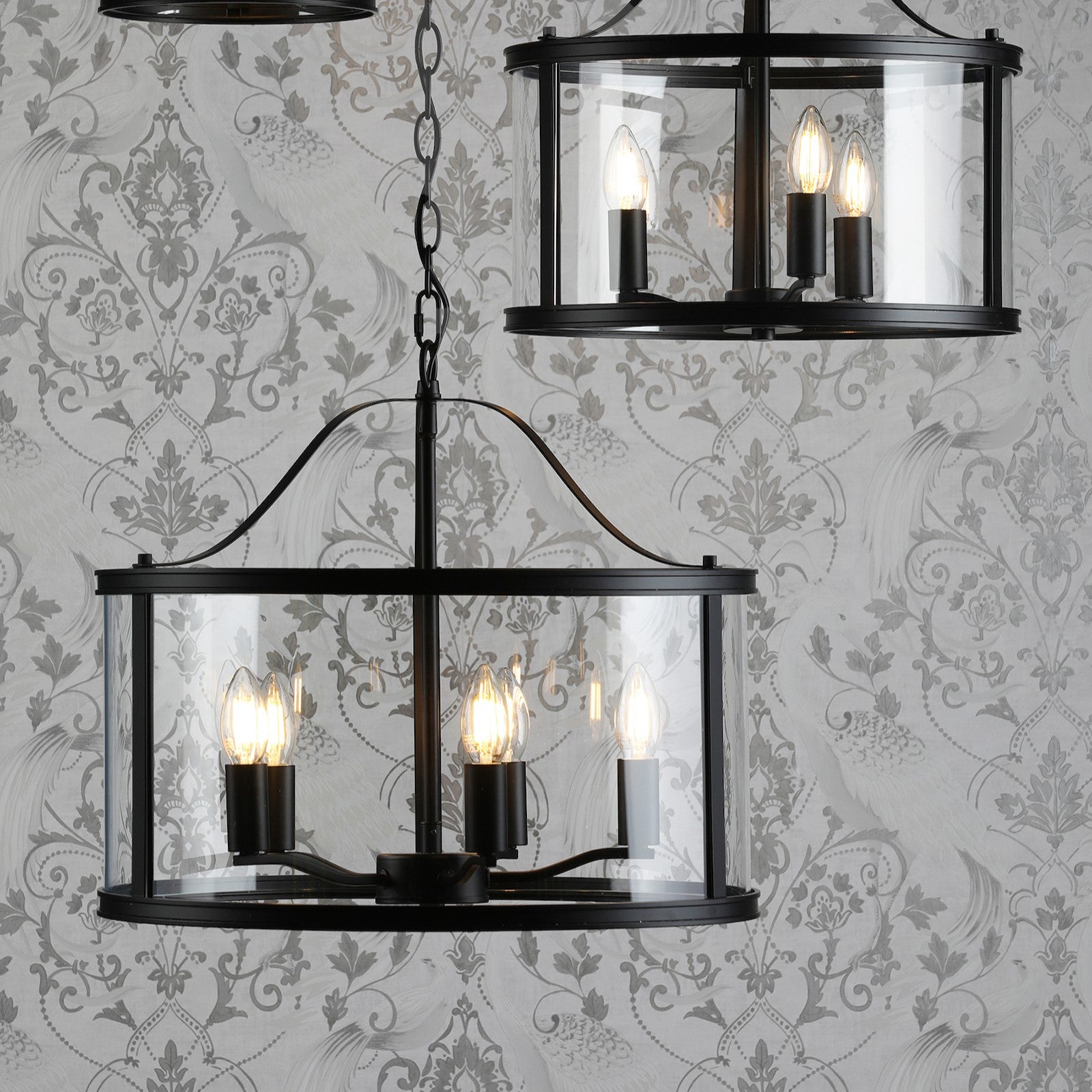 Two black chandeliers with glass panels hanging against a decorative gray and white wallpaper.