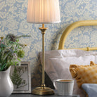 A brass table lamp with a pleated shade illuminating a cozy bedside scene.