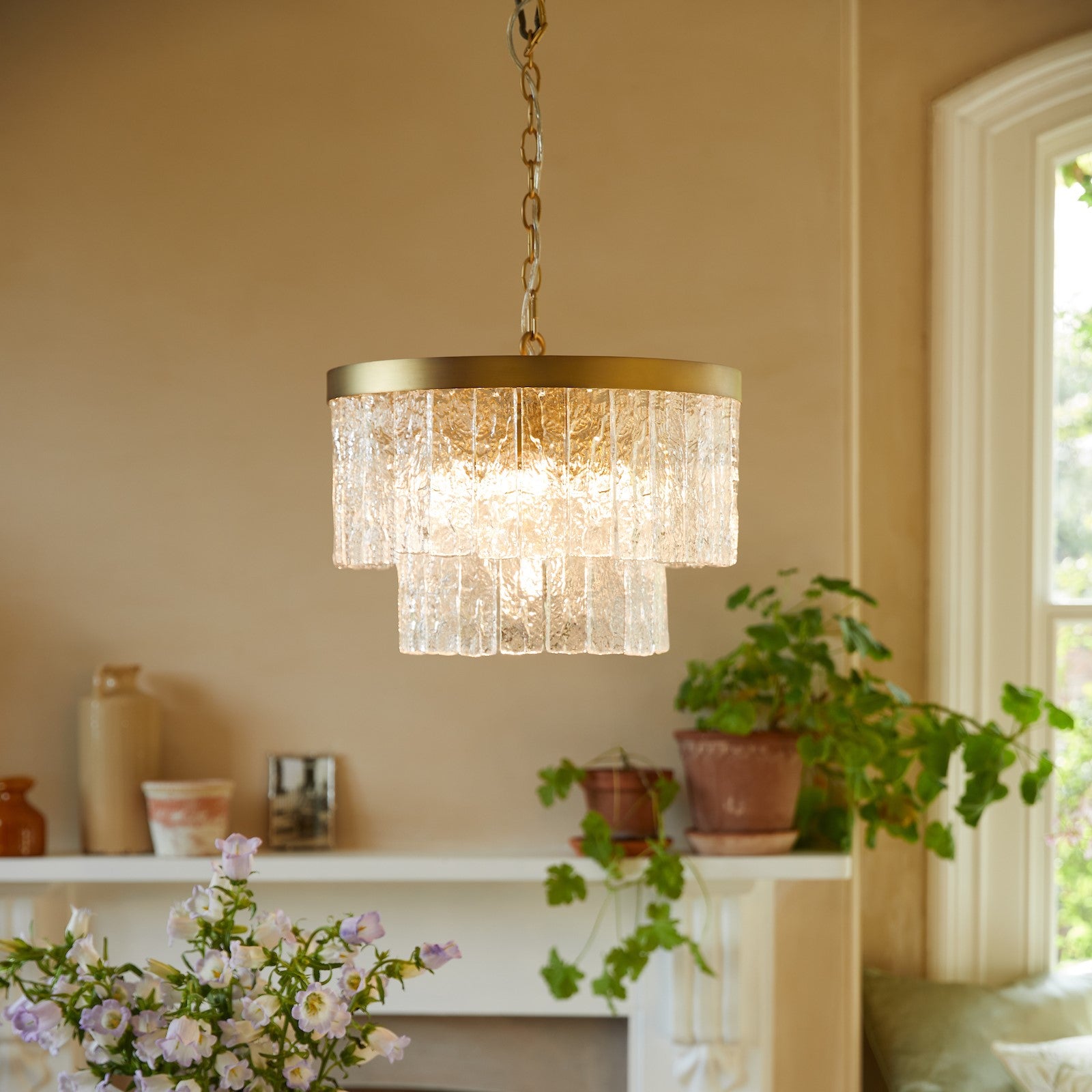 A two-tiered glass chandelier with a brass ring, illuminating a room with soft light.