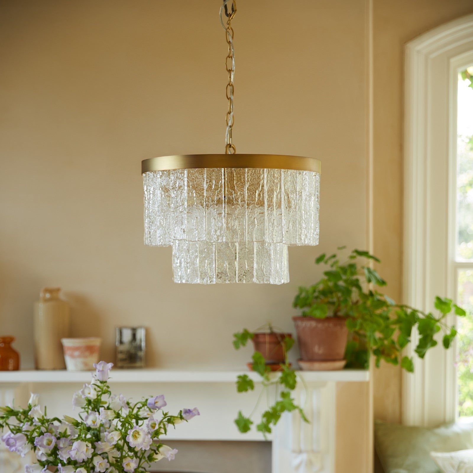 A two-tiered glass chandelier with a brass ring, hanging in a subtly lit room.