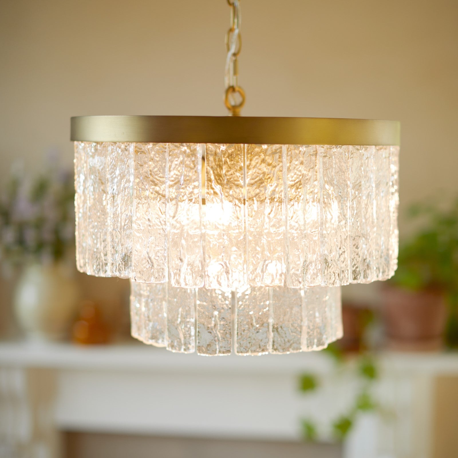 A close-up of a two-tiered glass chandelier with a brass ring, glowing brightly.