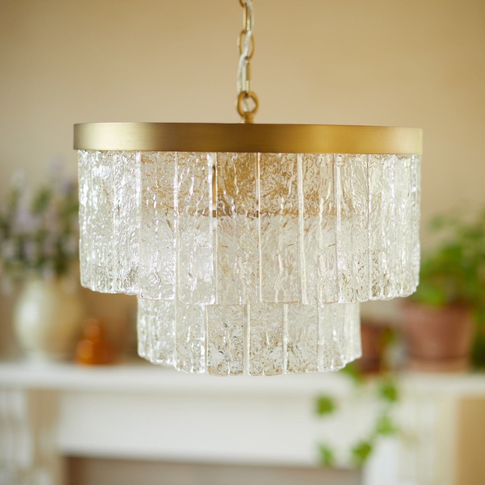 A close-up of a two-tiered glass chandelier with a brass ring, unlit.