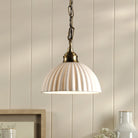 An ivory ceramic pendant light with a ribbed dome shade hangs from a brass chain.