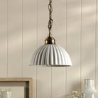 A white ceramic pendant light with a ribbed dome shade hangs from a brass chain.