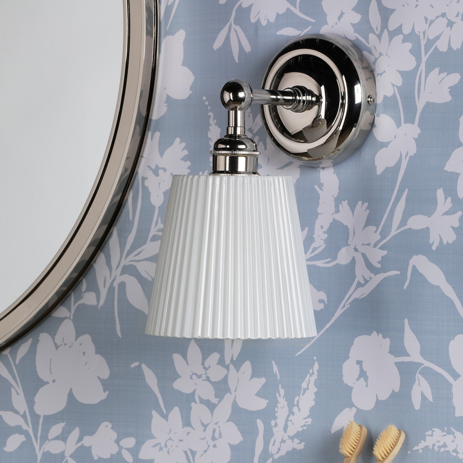 Polished nickel wall light with pleated shade in a bathroom with blue floral wallpaper.