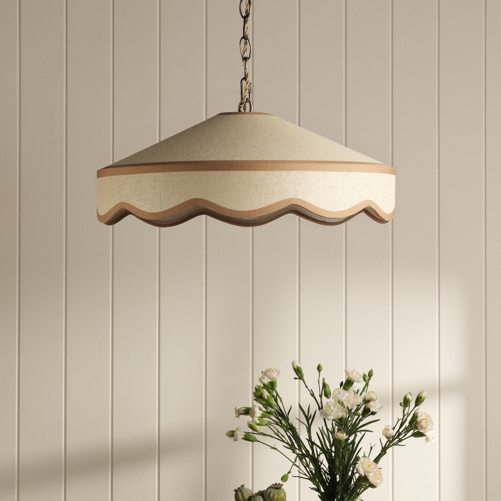 A hanging ceiling light with a cream-colored shade and a wavy trim in a room with white paneled walls.
