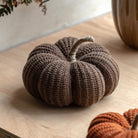 Brown knitted pumpkin with a natural stem, perfect for rustic autumn decor on a wooden surface.