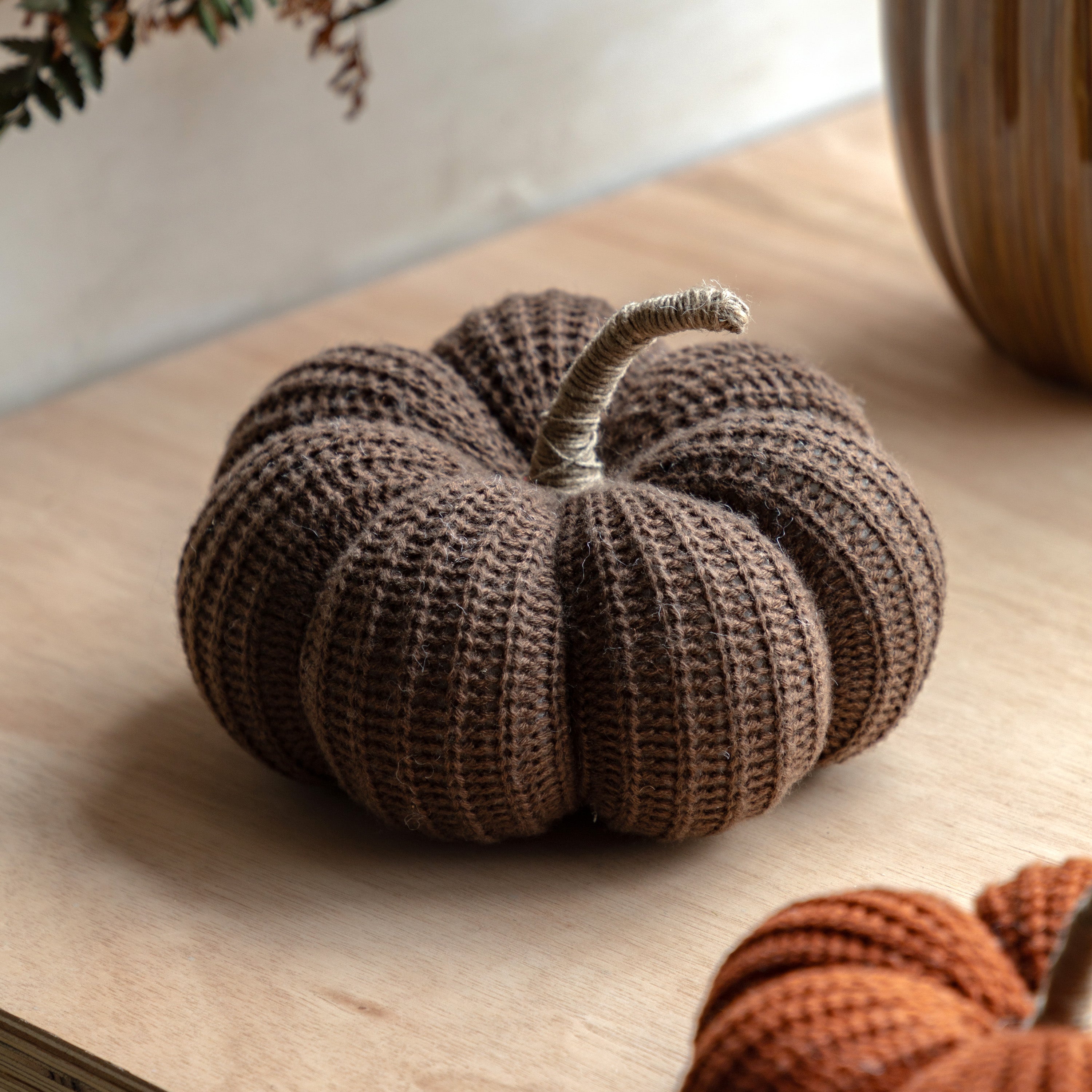 Brown knitted pumpkin with a natural stem, perfect for rustic autumn decor on a wooden surface.
