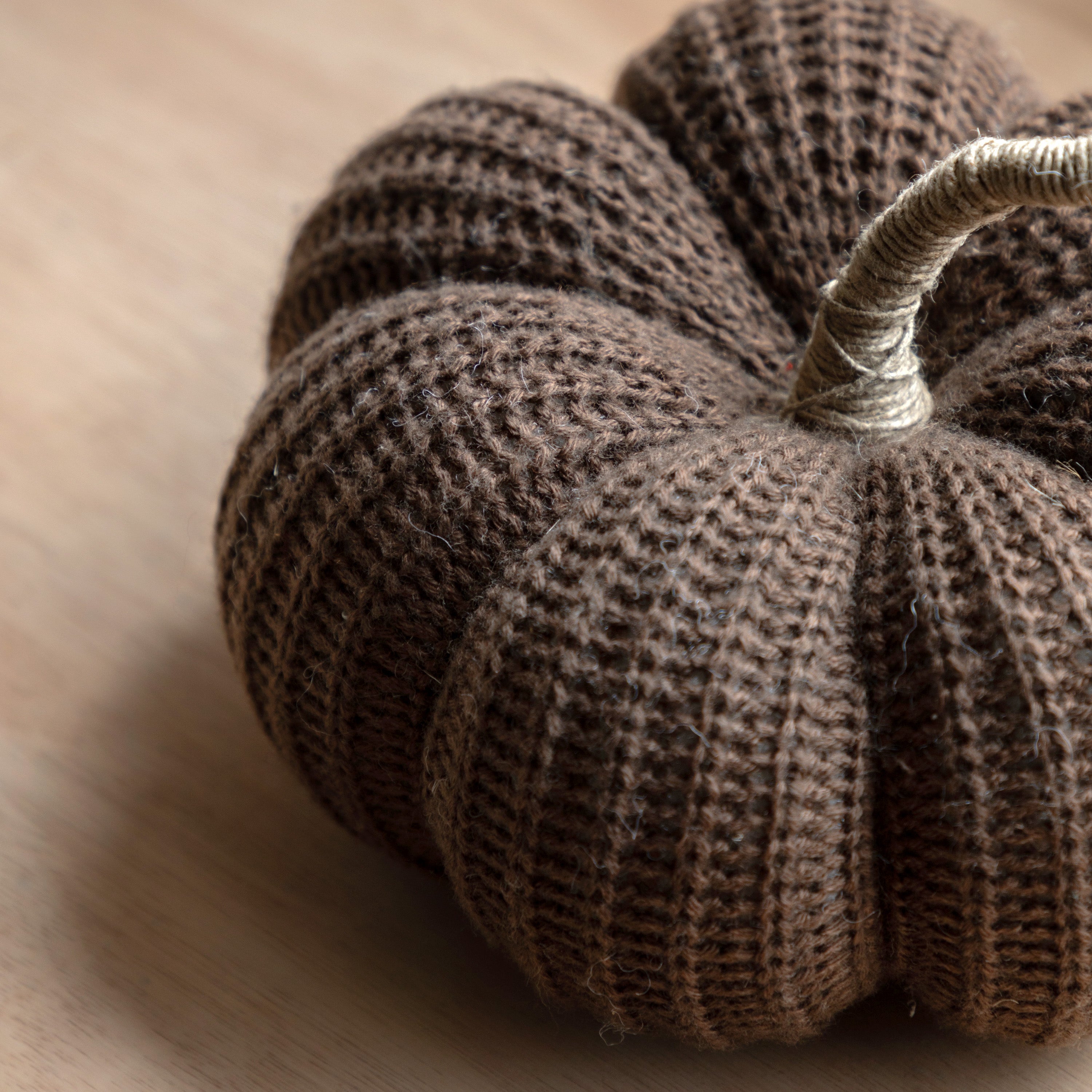 Close-up of a brown knitted pumpkin, showing textured yarn and a natural stem detail.