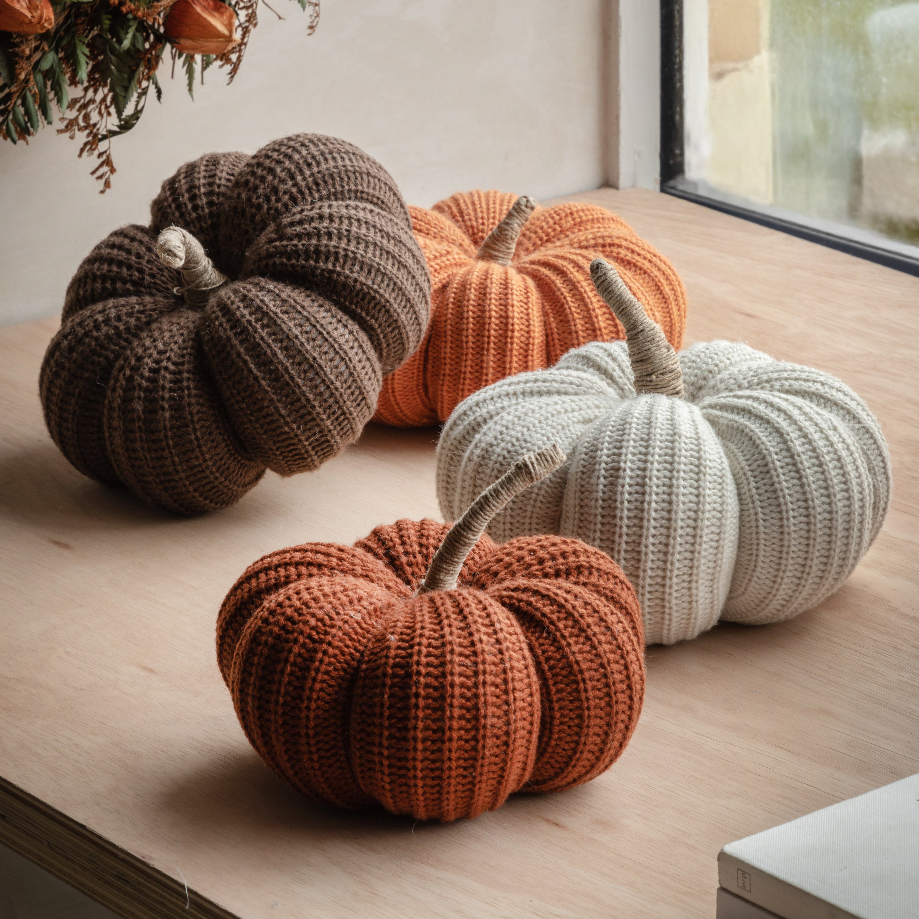 Collection of knitted pumpkins in brown, orange, and white, nestled on a windowsill.