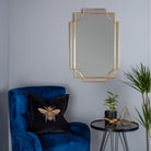 Florence Gold Ornate Wall Mirror hanging above a blue velvet chair with a bee cushion.