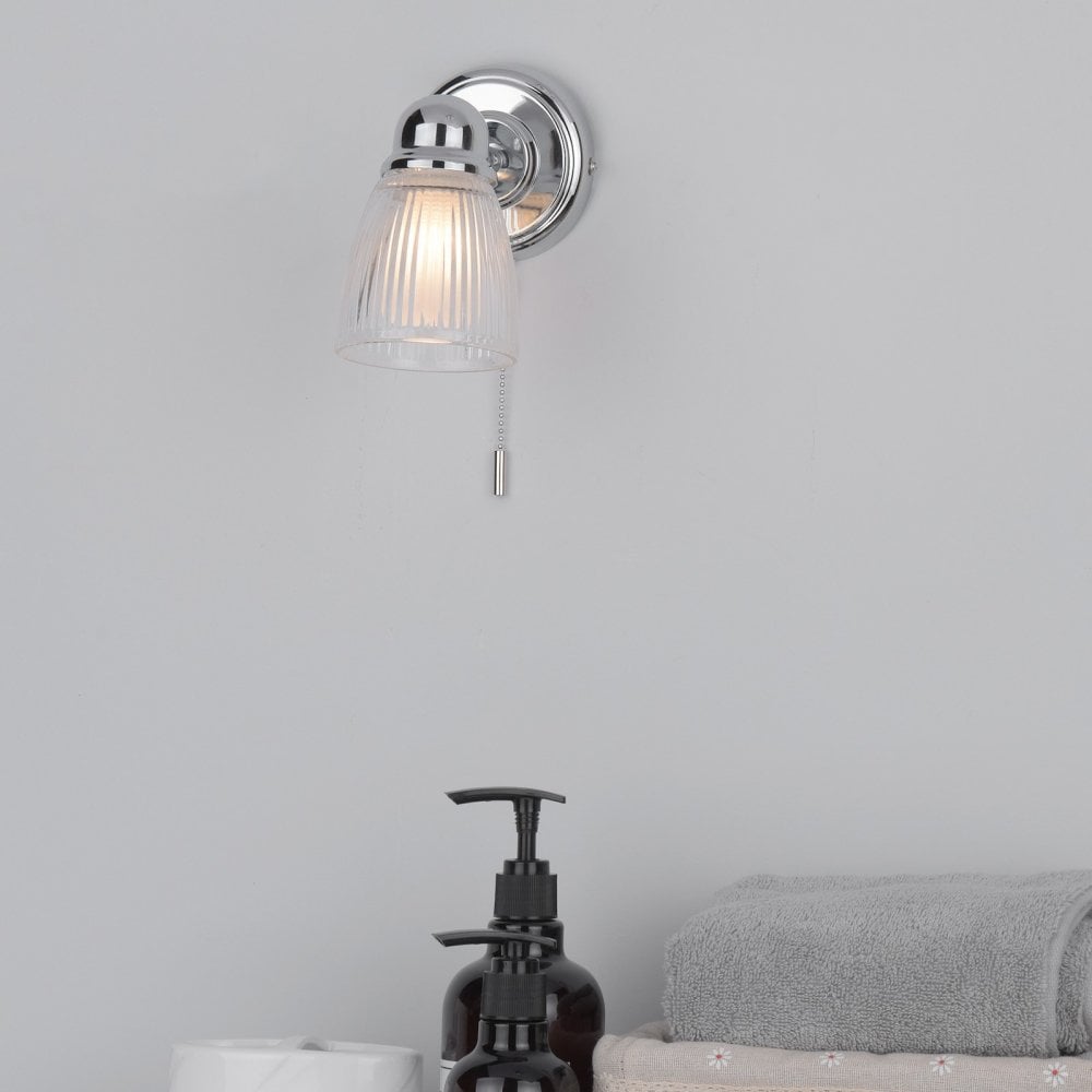 A lit wall light illuminates a bathroom scene with soap, towels, and toilet paper.