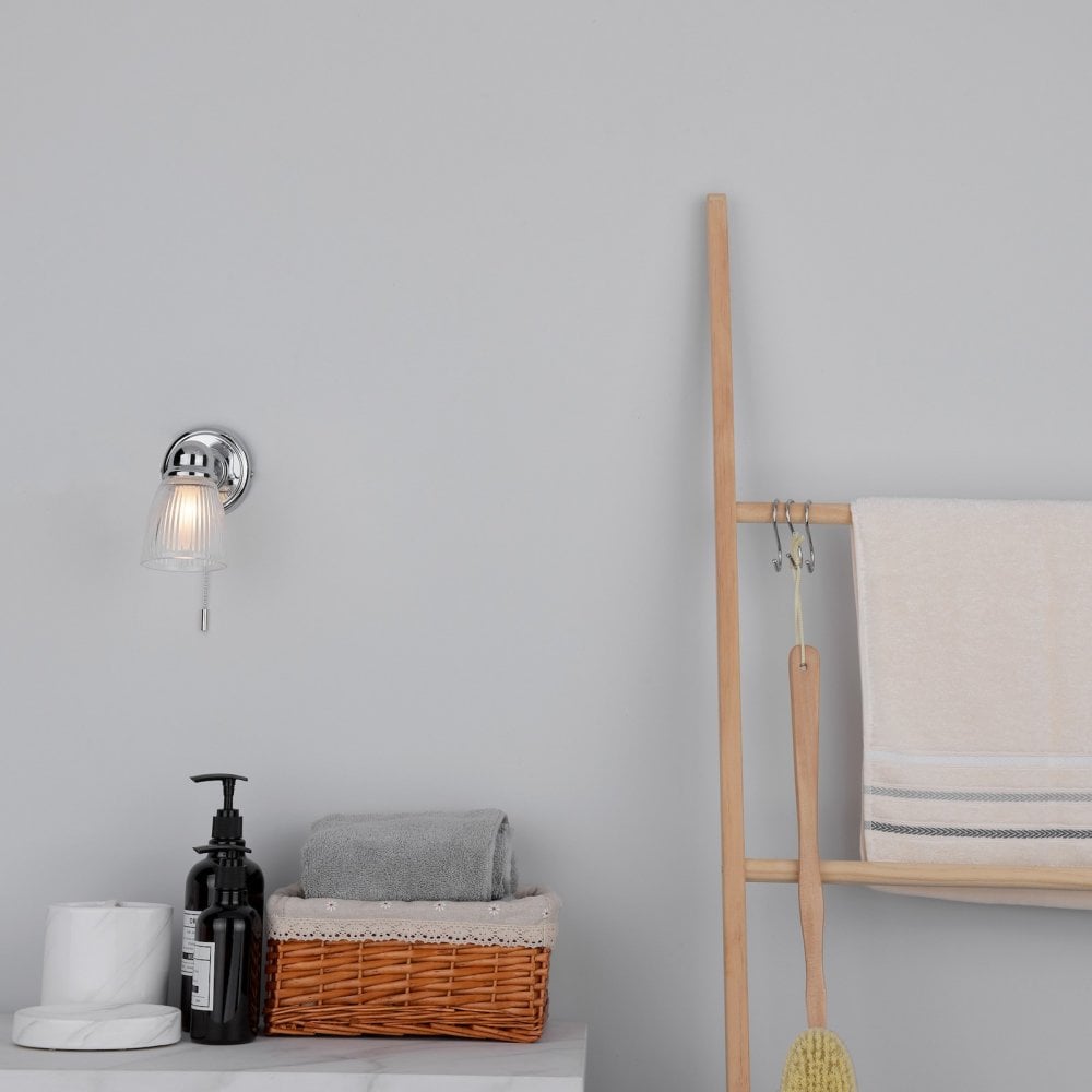 A lit wall light in a bright bathroom setting with wooden ladder and towels.