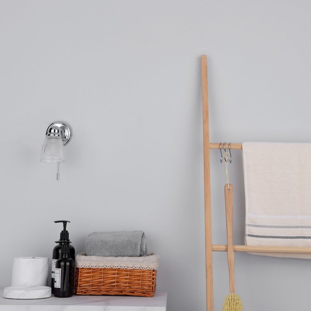 An unlit wall light in a bright bathroom setting with wooden ladder and towels.