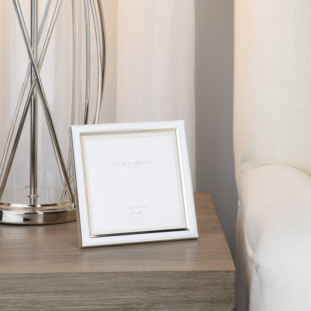 A white photo frame with a silver trim sits on a wooden bedside table.