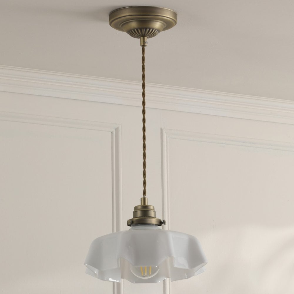 A brass pendant light with a white fluted glass shade hangs from a ceiling.