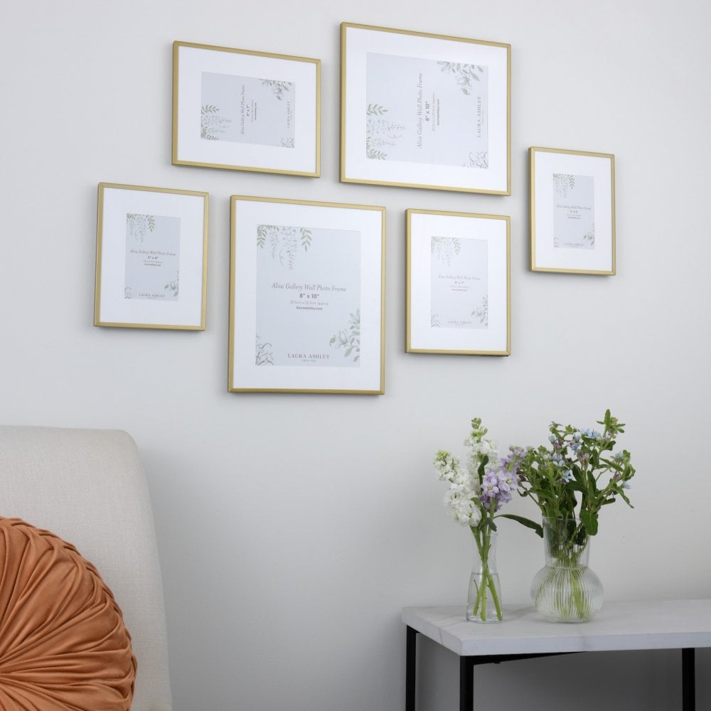 A gallery wall arrangement of six gold picture frames in various sizes on a white wall.