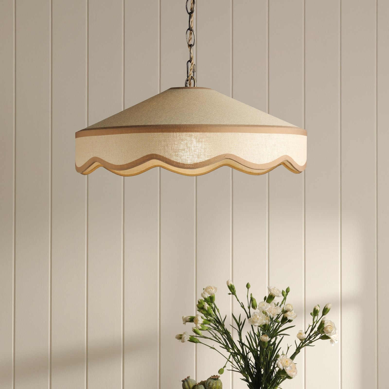 A hanging ceiling light with a cream-colored shade and a wavy trim in a room with white paneled walls.